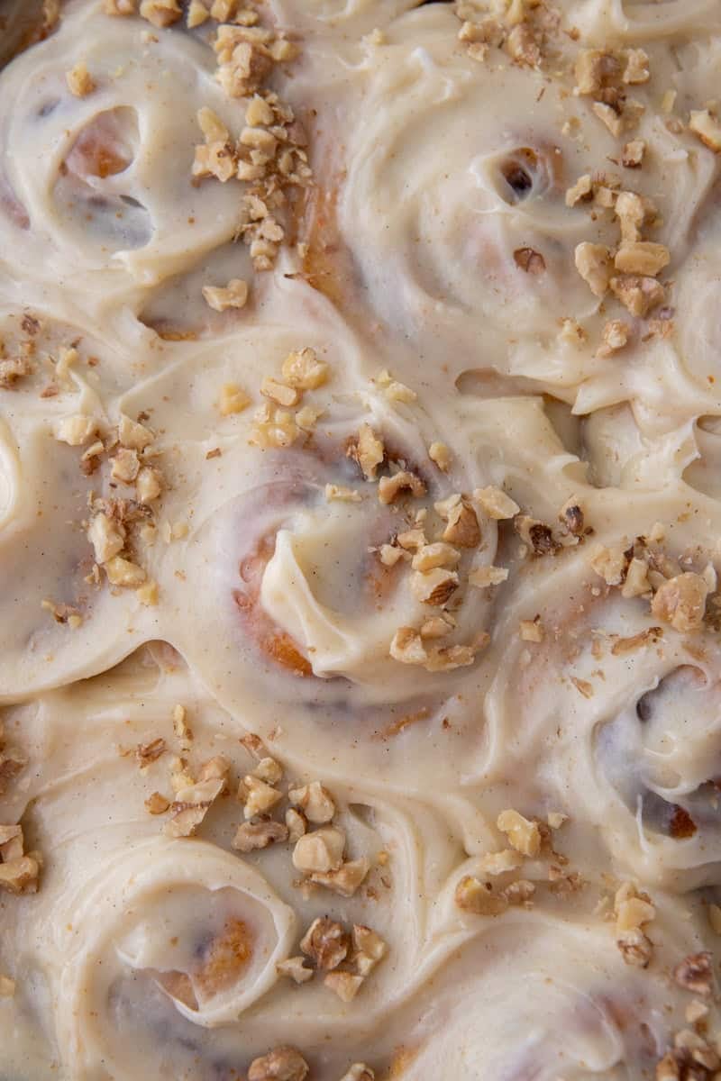 Close-up overhead of carrot cake cinnamon rolls covered in brown butter cream cheese frosting and topped with chopped walnuts