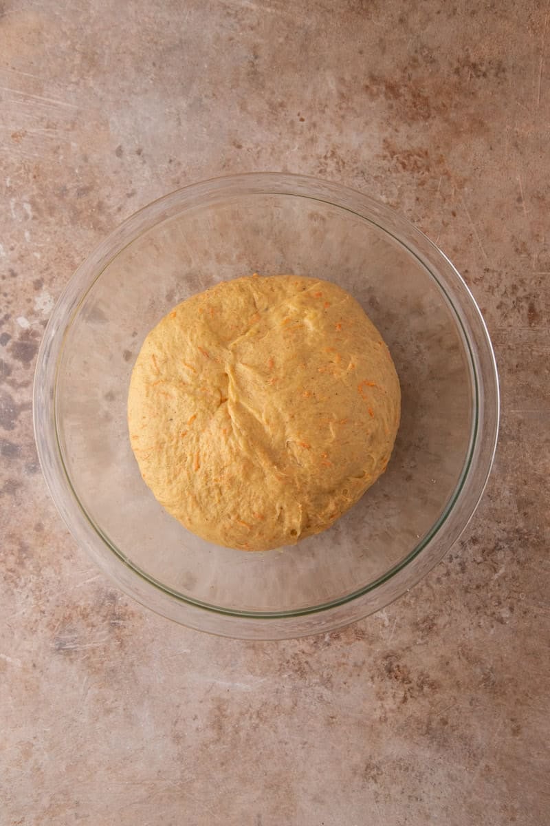 Cinnamon roll dough in a glass bowl before rising, with visible orange flecks from shredded carrots