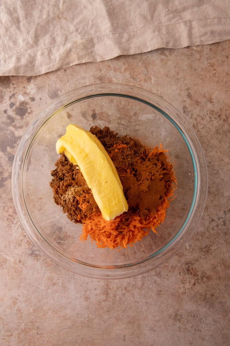Softened butter, brown sugar, shredded carrots, and cinnamon in a glass bowl before mixing the carrot cake filling