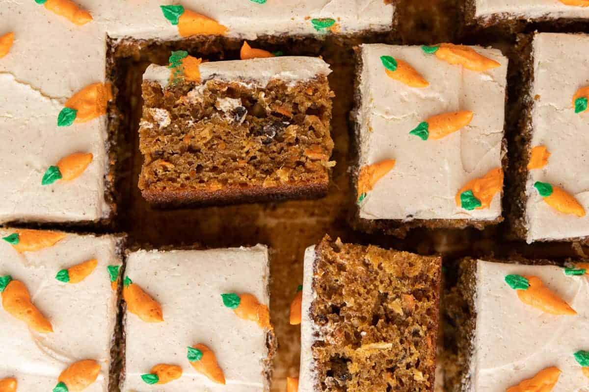 Moist carrot cake sheet cake cut into squares with cream cheese frosting and piped carrot decorations in a 9 by 13 pan
