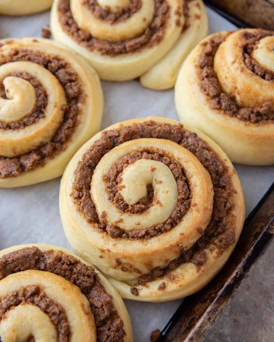 Freshly baked cookie butter cinnamon rolls with golden caramelized edges on a sheet pan