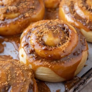 Cookie butter cinnamon roll topped with molten Biscoff glaze dripping down the sides on a sheet pan