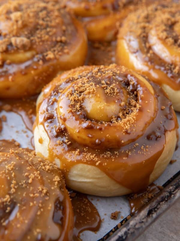 Cookie butter cinnamon roll topped with molten Biscoff glaze dripping down the sides on a sheet pan