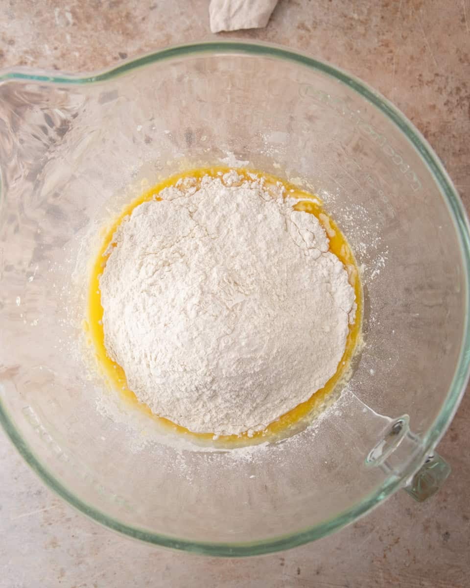 Flour mounded over the wet ingredients in a glass bowl before mixing the cinnamon roll dough