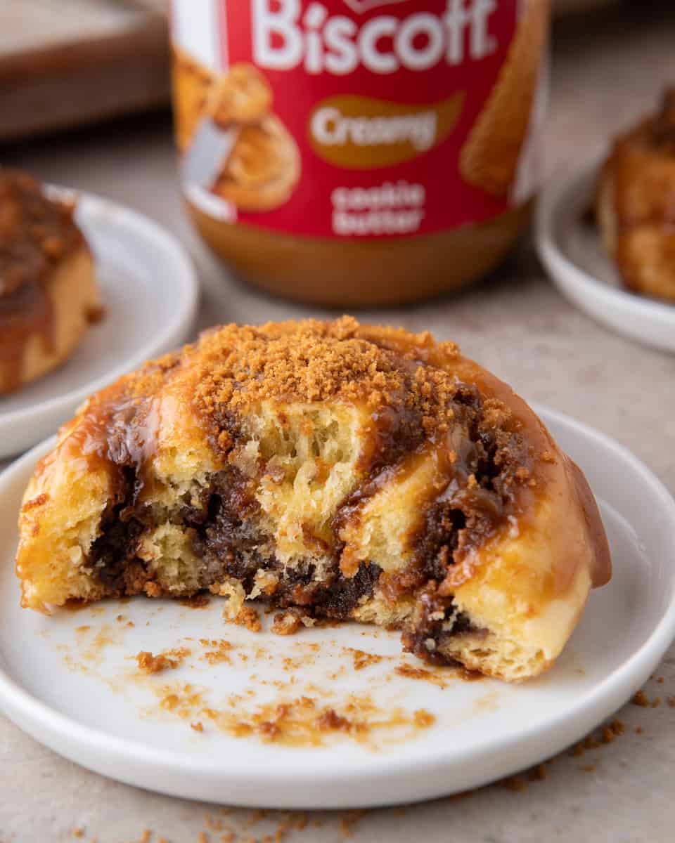 Cookie butter cinnamon roll on a white plate with a bite taken, showing the gooey Biscoff swirl inside