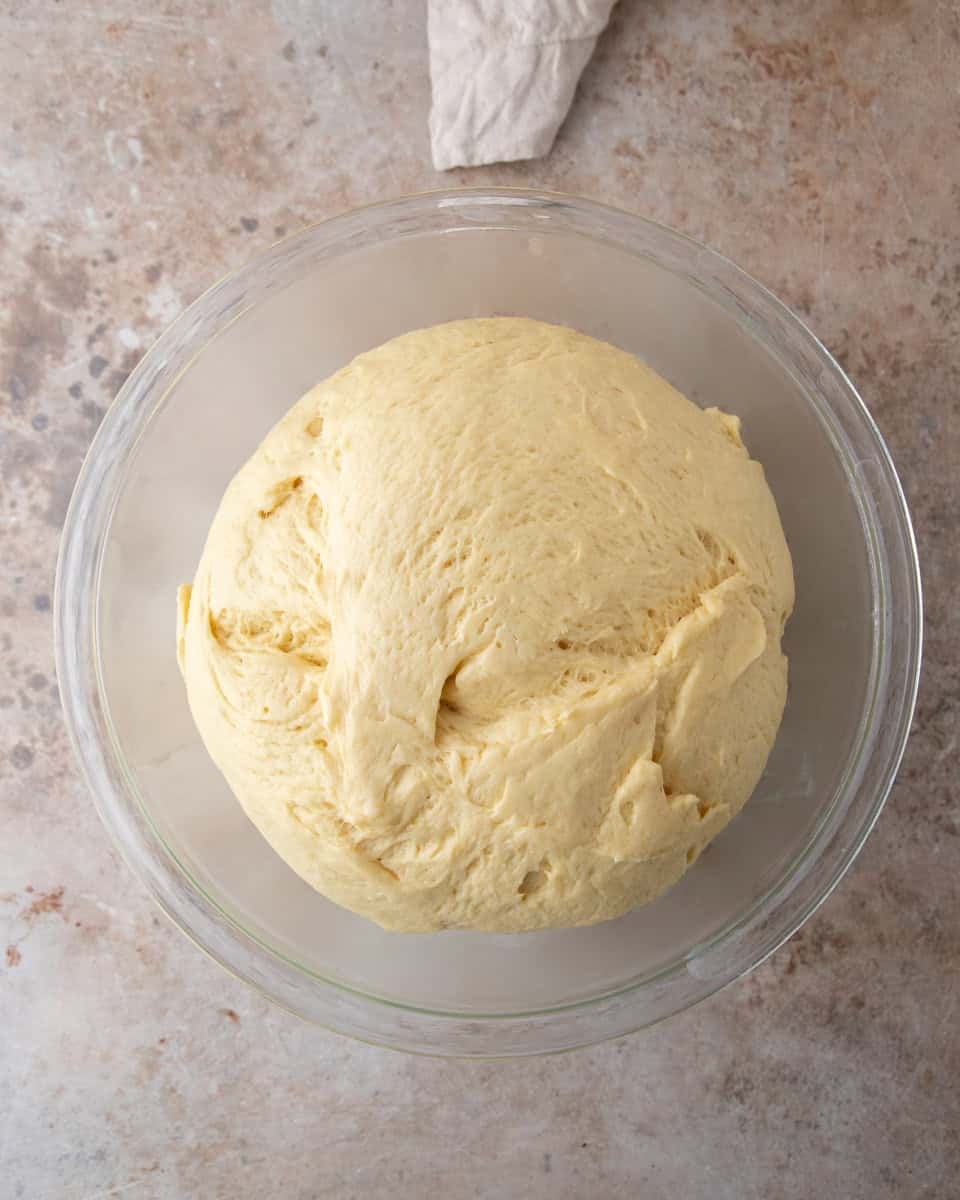 Brioche dough doubled in size in a glass bowl after the first rise
