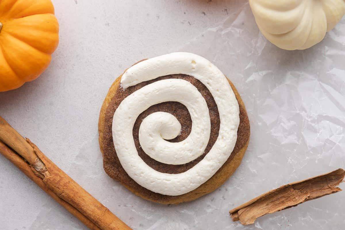 Crumbl pumpkin roll cookie with cream cheese frosting and mini pumpkins