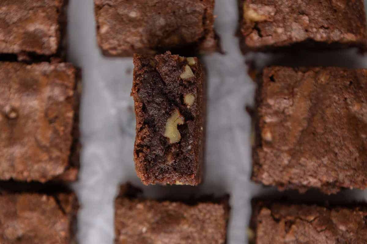 Fudge walnut brownies sliced into squares with one piece tilted showing the dense chocolate interior studded with chopped walnut pieces