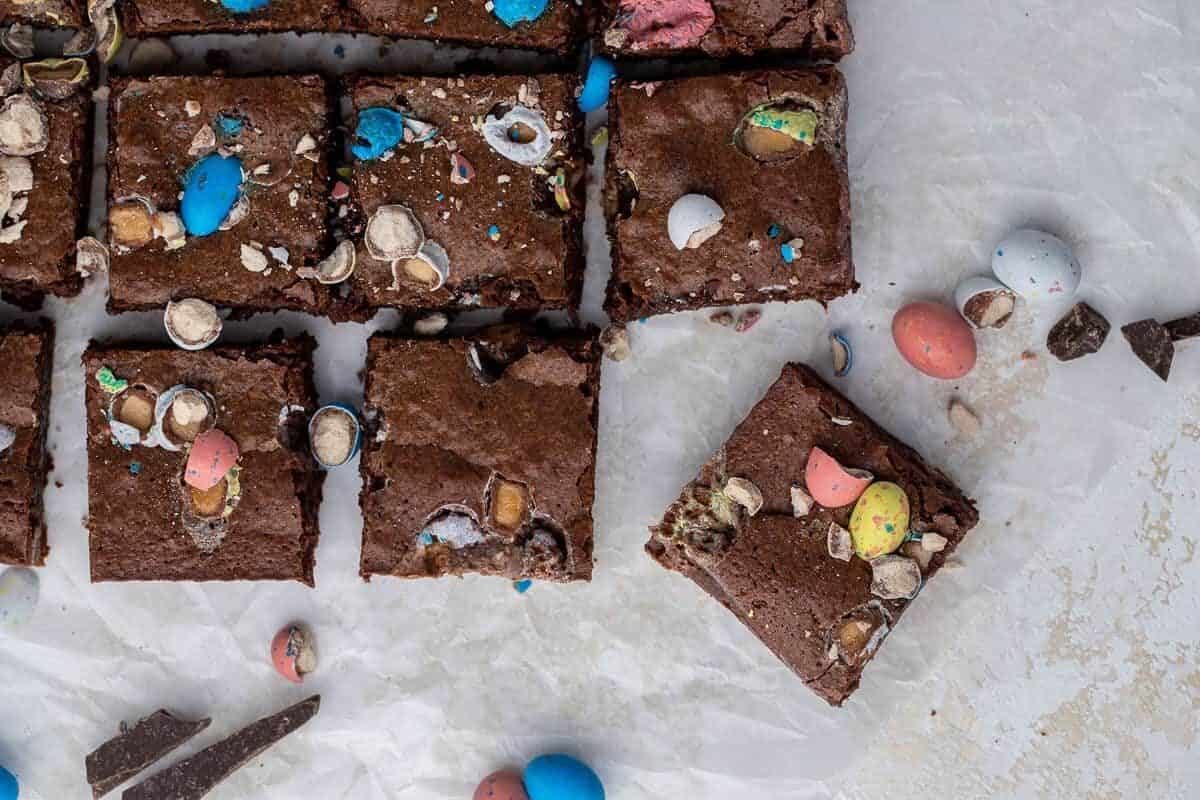 Overhead view of fudgy Easter mini egg brownies sliced into squares on parchment paper topped with crushed colorful Cadbury Mini Eggs and Robin Eggs
