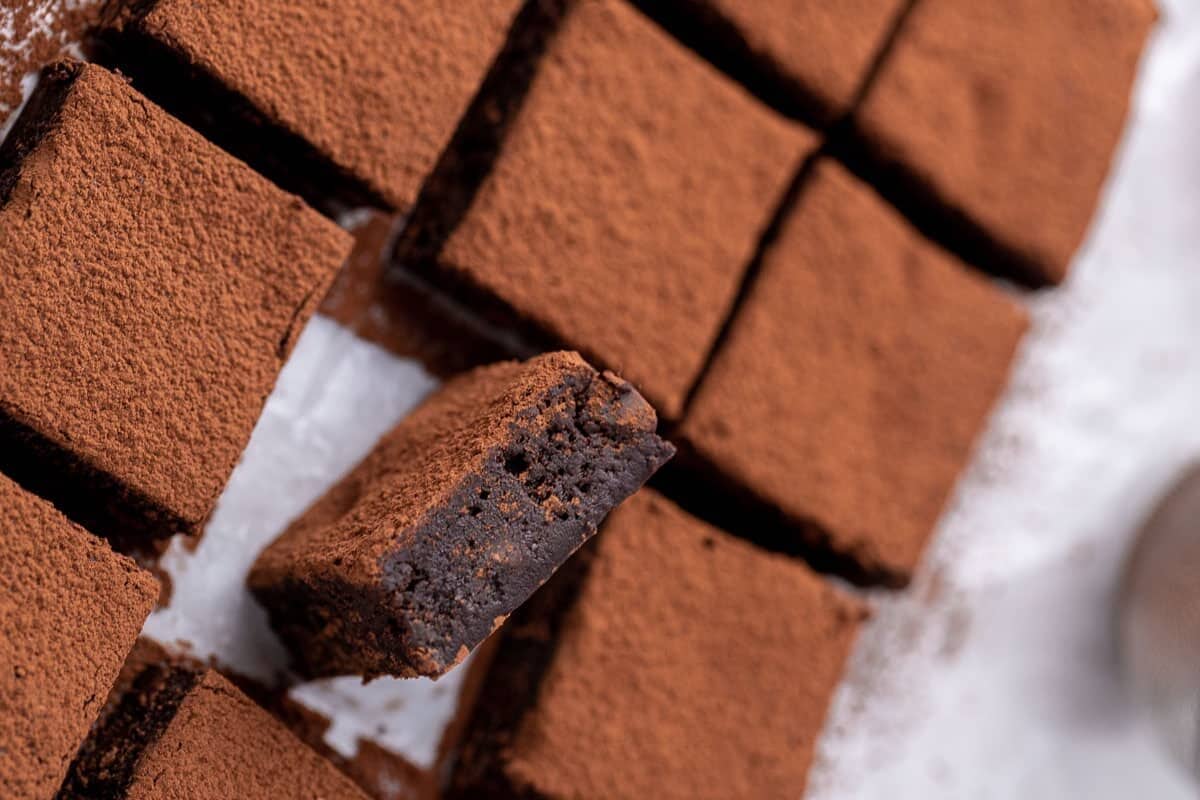 Red wine brownies dusted with cocoa powder sliced into squares with one piece tilted to show the dense fudgy chocolate center