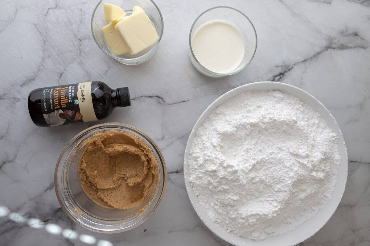 brown butter frosting ingredients on a marble surface including browned butter powdered sugar heavy cream and vanilla extract