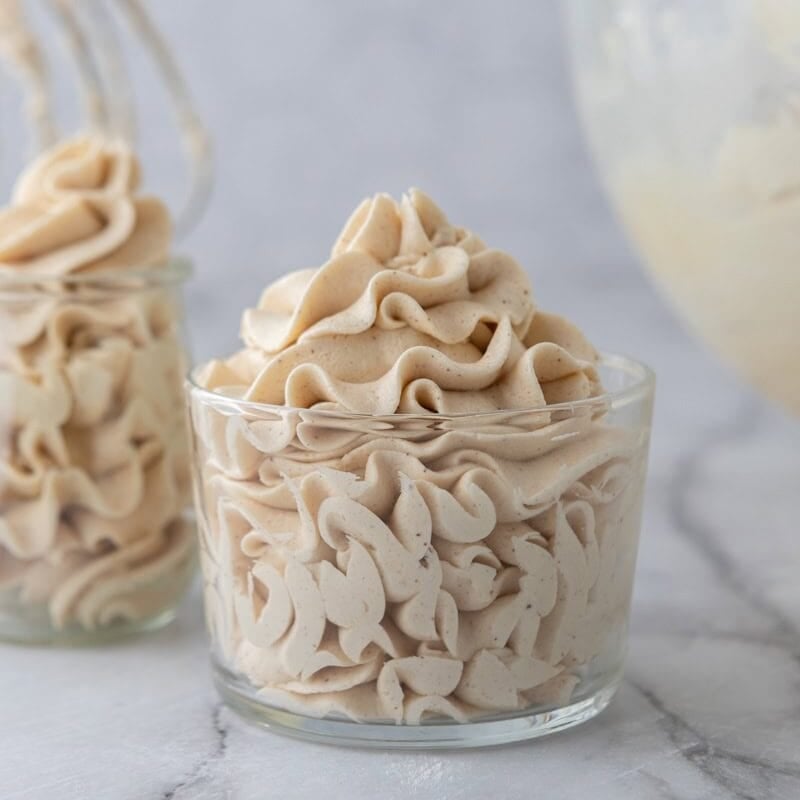 brown butter frosting piped in ruffles into a clear glass bowl with a second jar in the background