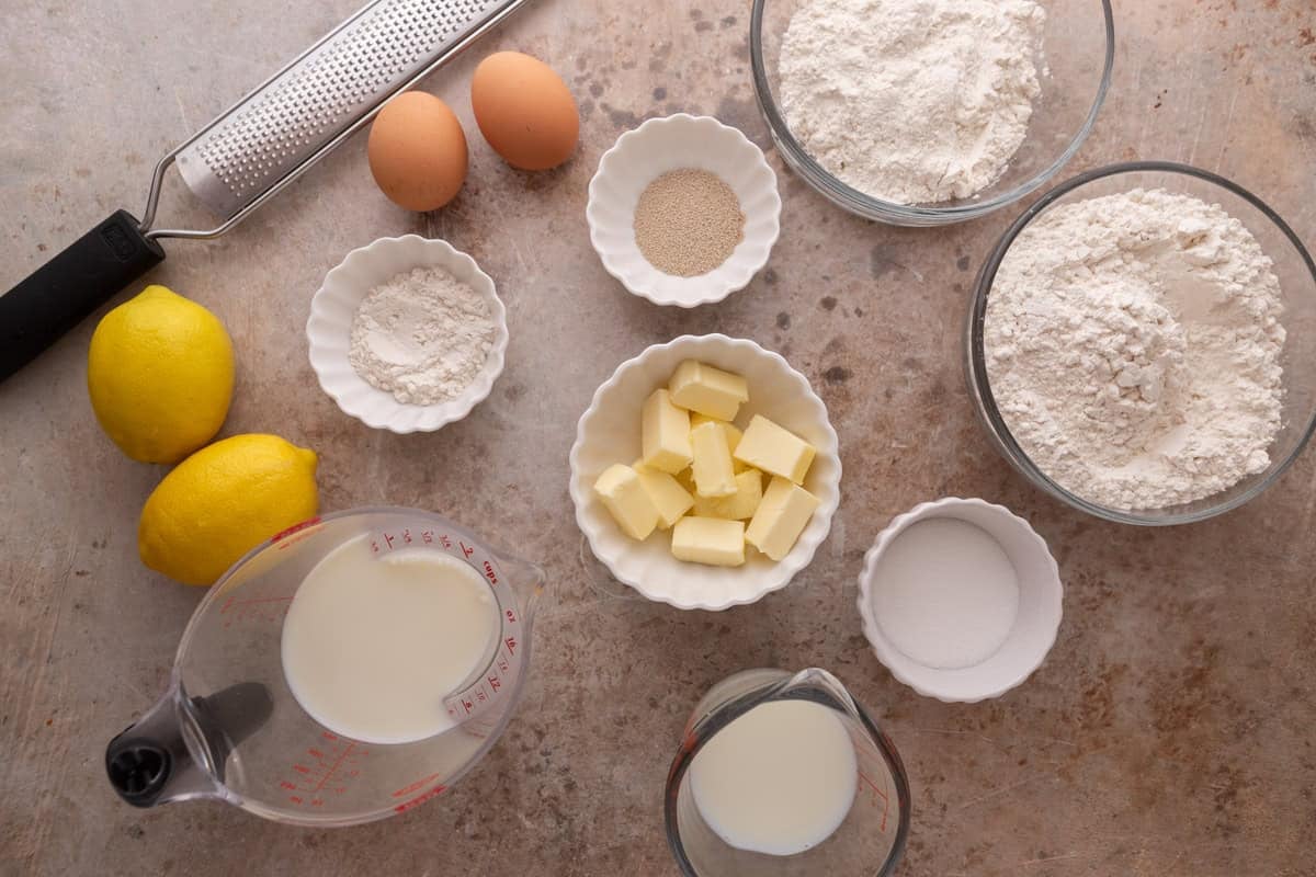 Flatlay of dough ingredients including eggs, yeast, flour, butter, milk and lemons