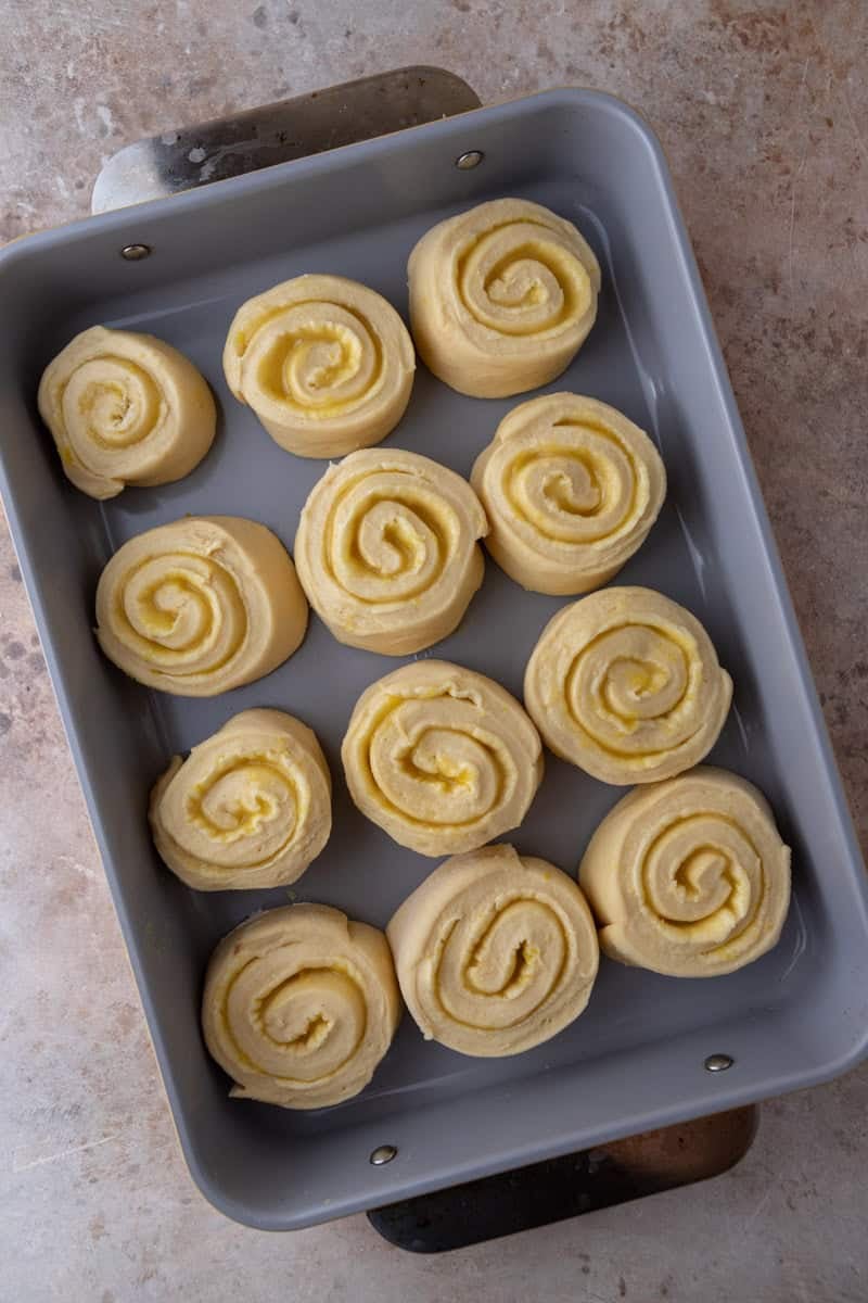 12 sliced lemon cinnamon rolls arranged in a grey baking pan before second rise