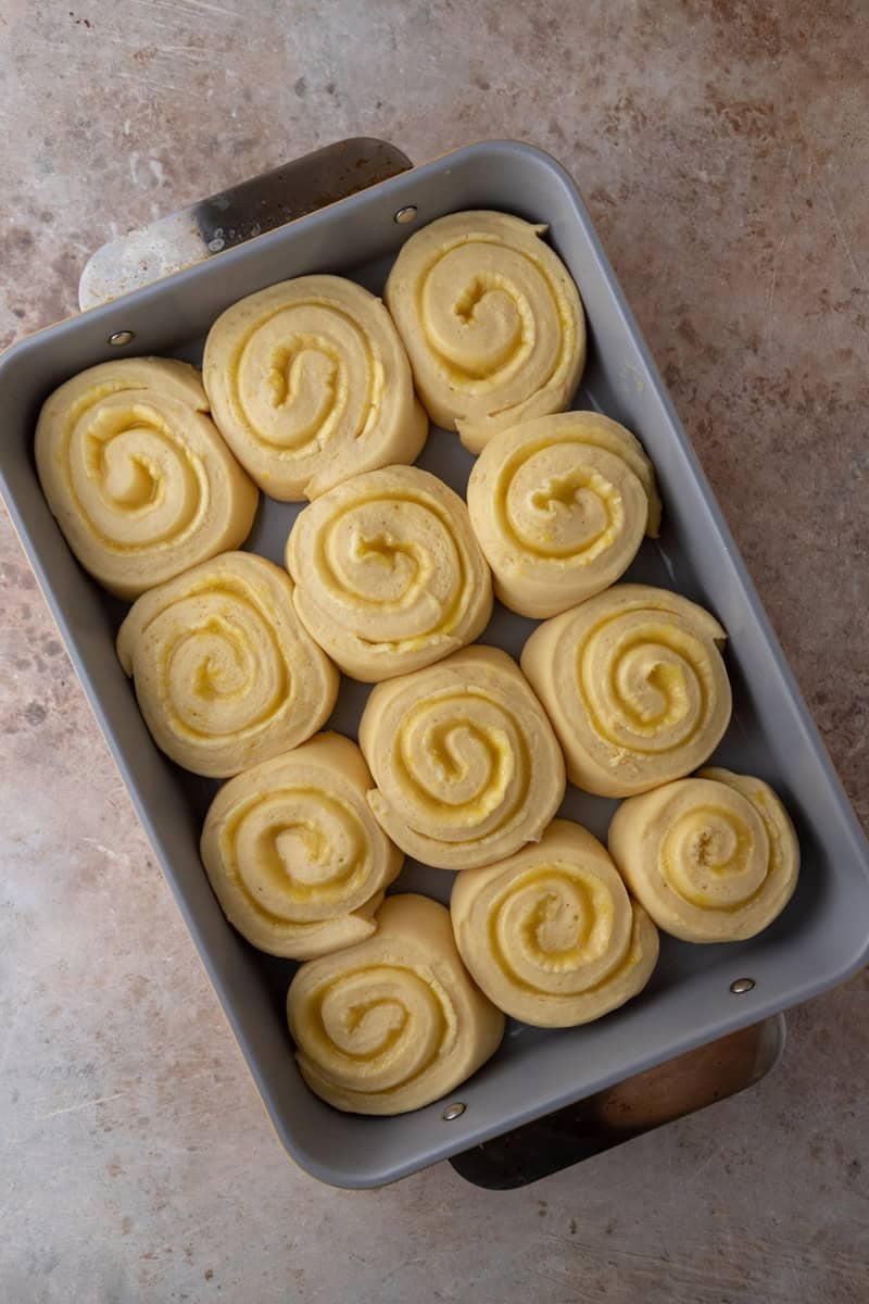 Lemon cinnamon rolls proofed and puffed in a grey baking pan ready to go in the oven