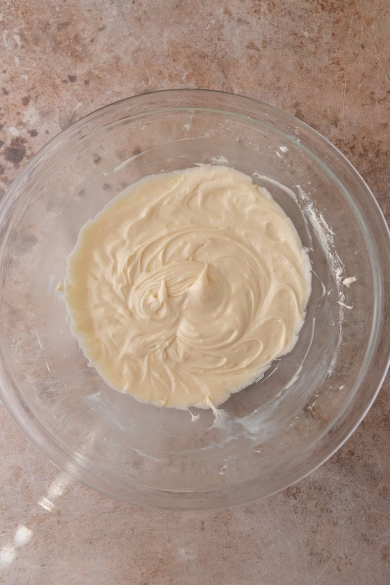 Smooth creamy lemon cream cheese frosting in a glass bowl ready to spread on lemon rolls