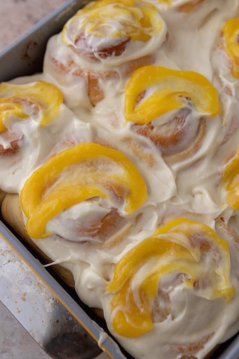 Pan of lemon rolls covered in cream cheese frosting with lemon curd swooped on top of each roll