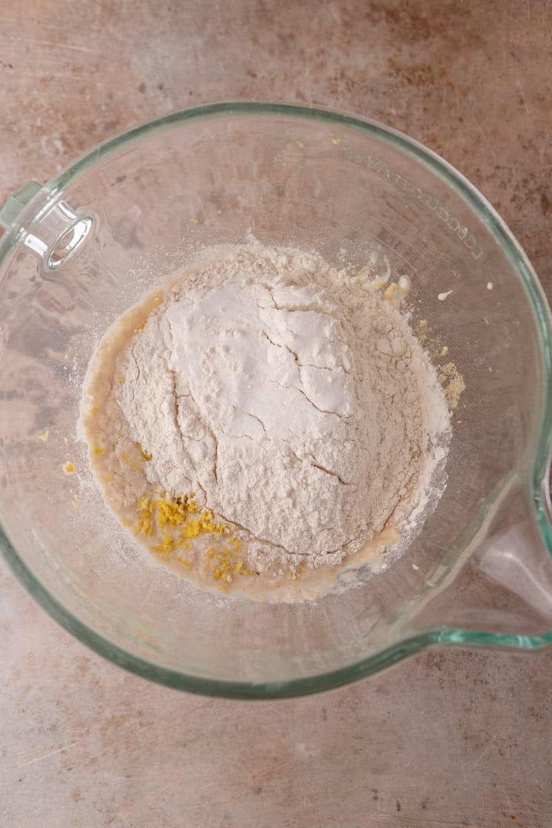 Flour added to lemon roll dough ingredients in a large glass bowl