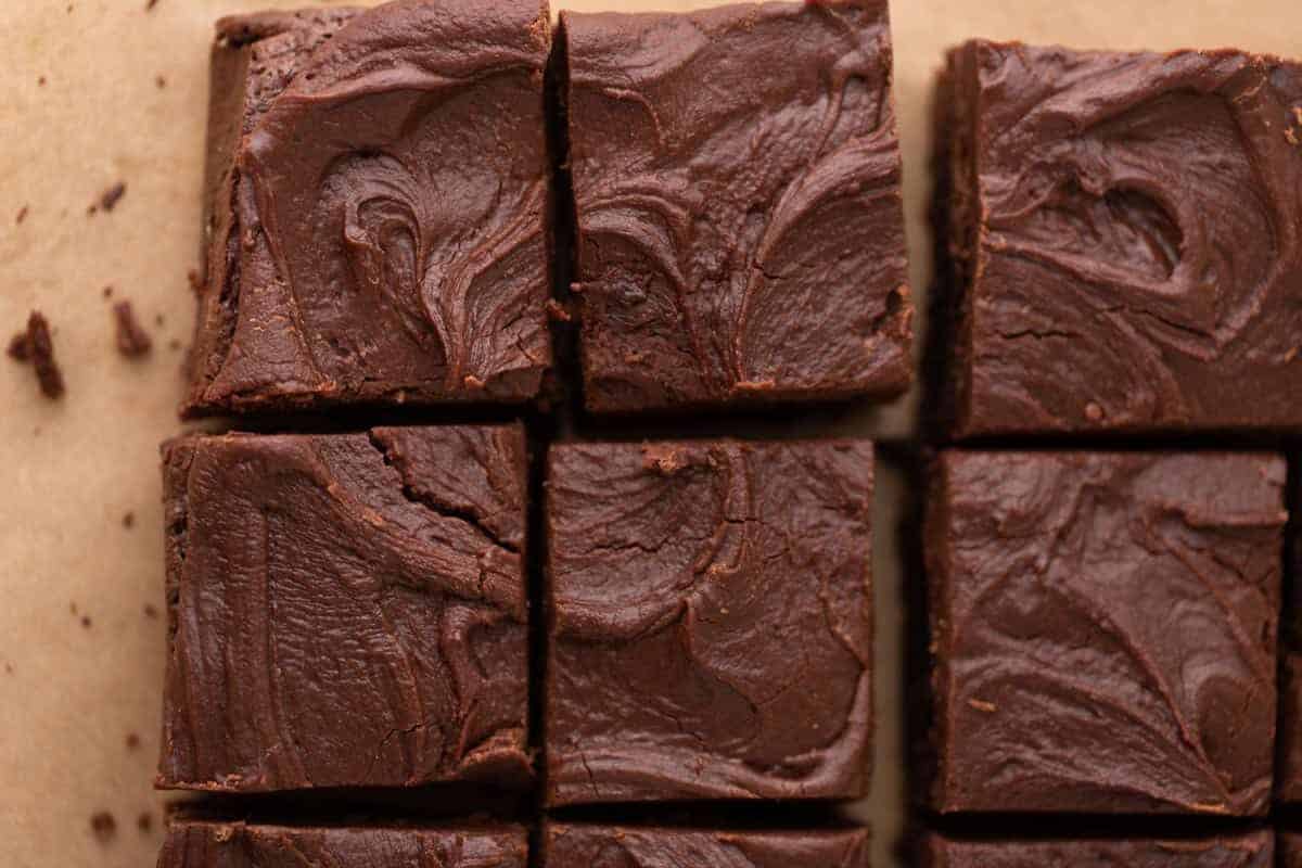Brownies topped with thick swirled chocolate brownie frosting sliced into squares on parchment paper showing the rich fudgy frosting layer