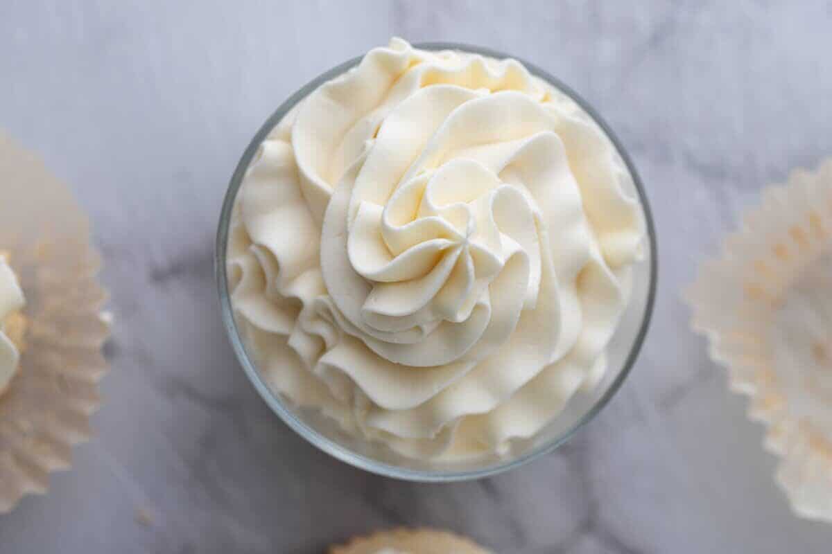 Overhead view of mascarpone frosting piped into a glass bowl surrounded by empty cupcake liners