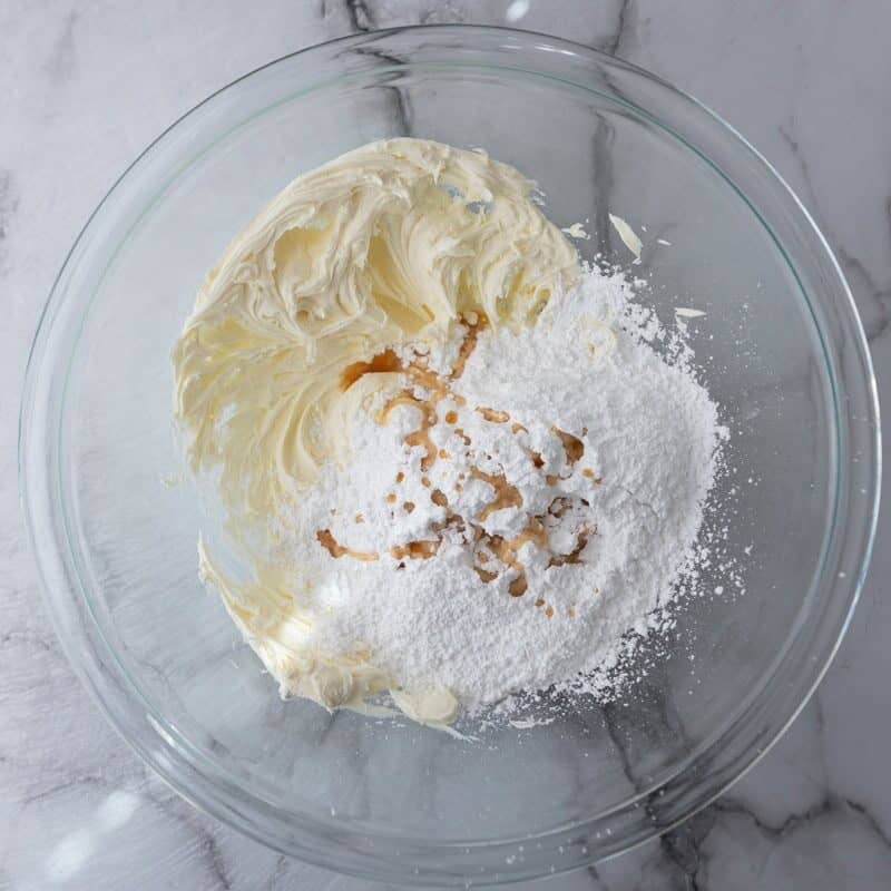 Mascarpone cheese and powdered sugar in a glass mixing bowl before being combined