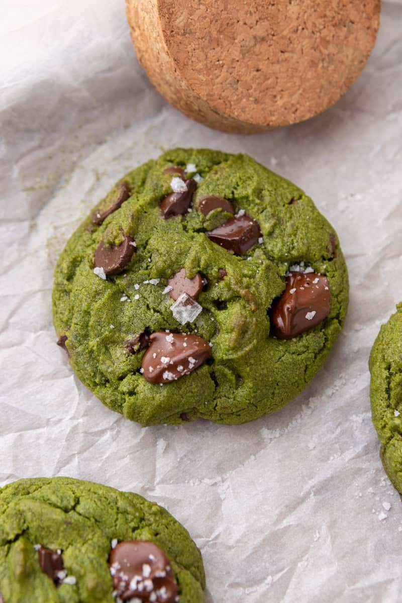 Close-up overhead of a baked matcha cookie topped with melted chocolate chunks and flaky sea salt