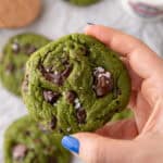 Hand holding a thick green matcha cookie with melty chocolate chunks and flaky sea salt on top