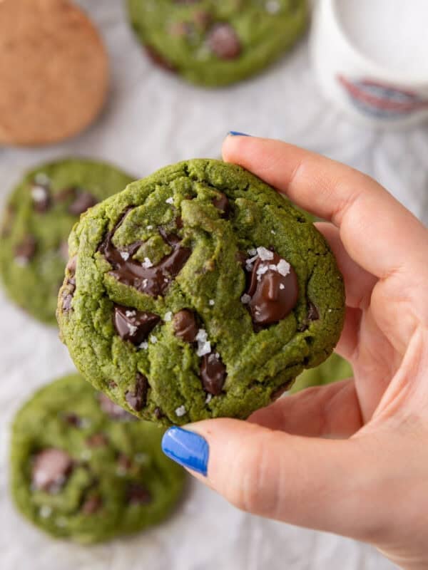 Hand holding a thick green matcha cookie with melty chocolate chunks and flaky sea salt on top