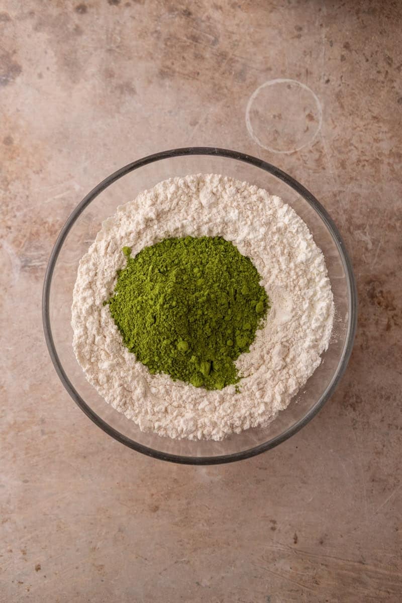 Vibrant green matcha powder on top of flour in a glass bowl before whisking the dry ingredients together
