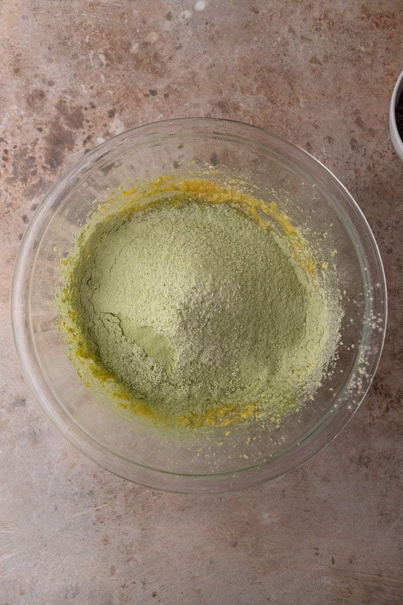 Matcha flour mixture added to the wet ingredients in a glass mixing bowl before combining