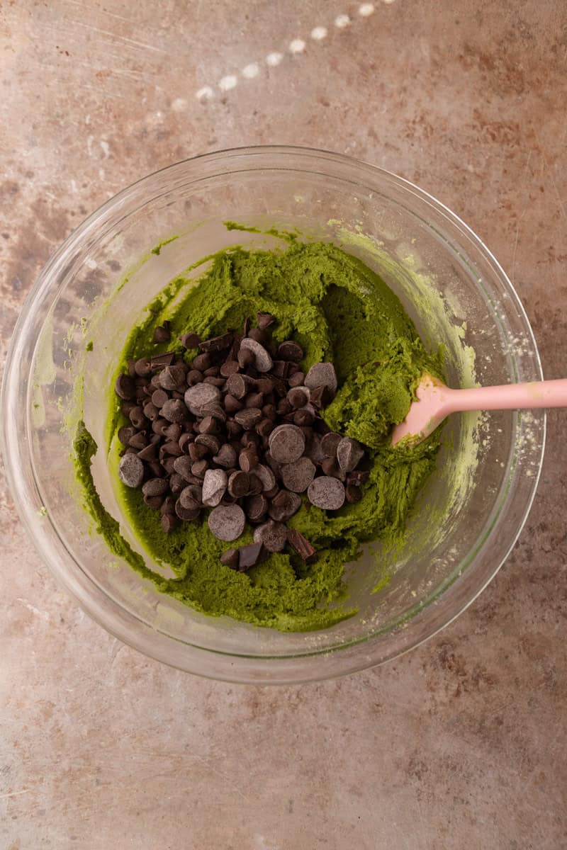 Bright green cookie dough with semi-sweet chocolate chips being folded in with a pink spatula