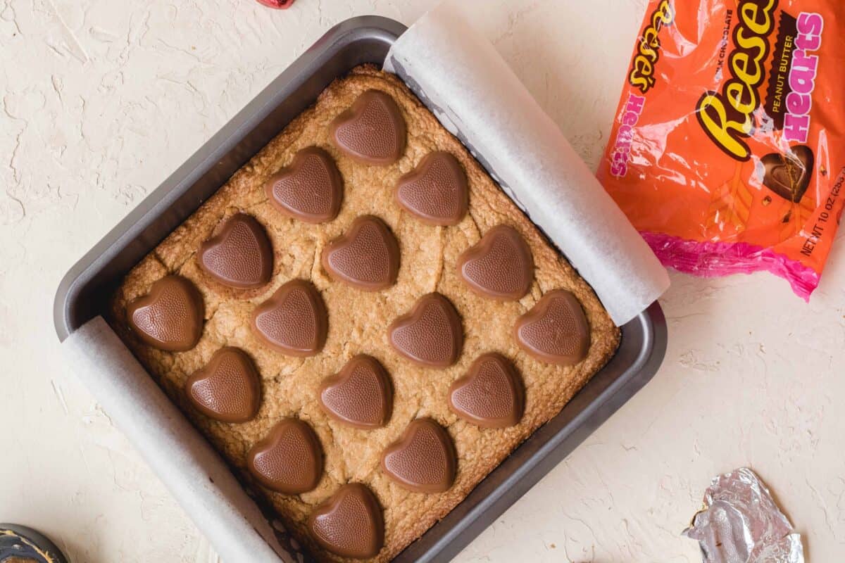 Peanut butter blondies in a baking pan topped with Reese's peanut butter hearts next to the candy bag
