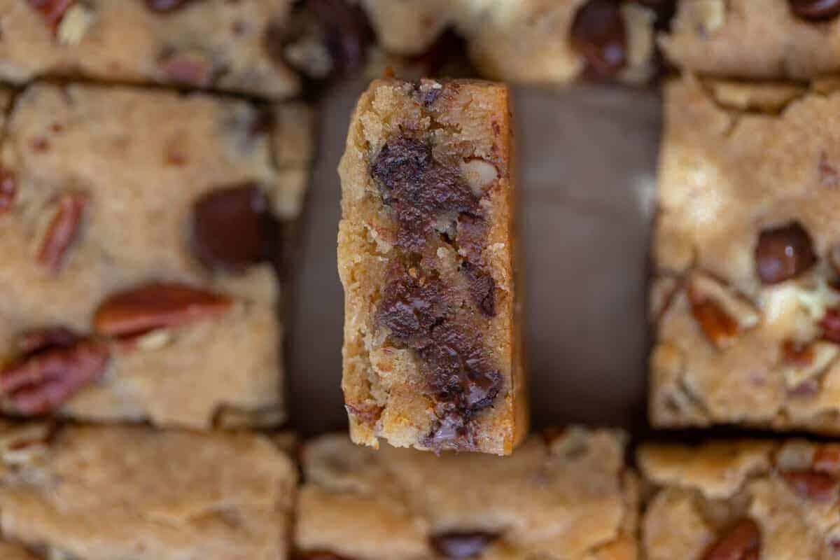 Chewy pecan chocolate chip blondies sliced into bars with one piece tilted to show the fudgy interior studded with melted chocolate and crunchy pecans