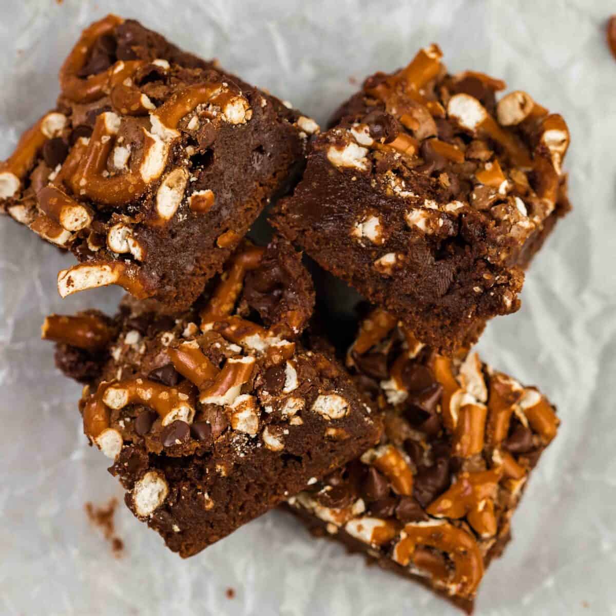 Pretzel brownies piled together showing crushed pretzels and chocolate chips baked into the fudgy chocolate brownie base on parchment paper