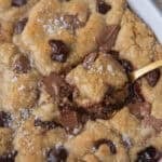 Scoopable chocolate chip cookie with molten chocolate center being scooped from a baking dish