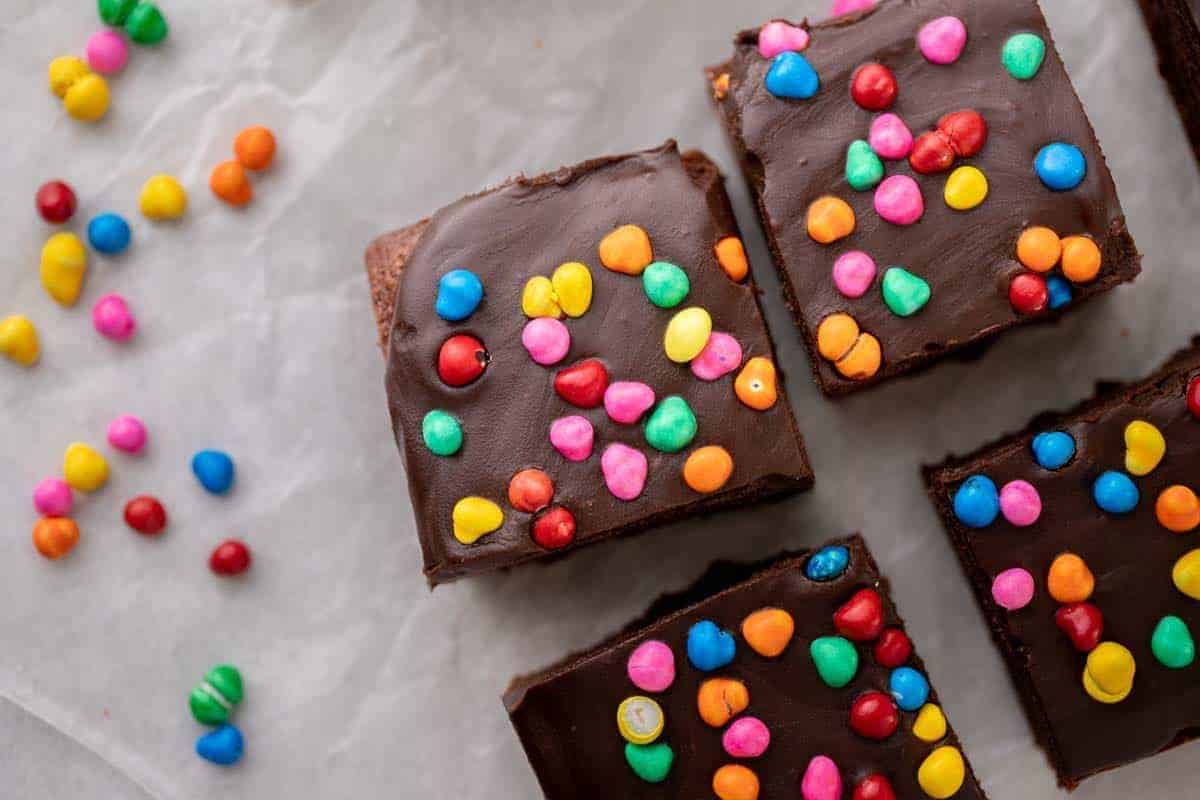 Homemade cosmic brownies topped with thick chocolate ganache and colorful rainbow candy chips on parchment paper