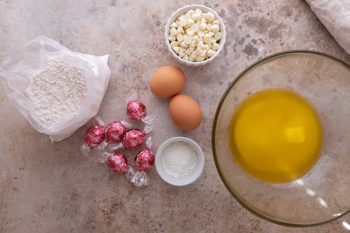 Ingredients laid out on a marble surface including cake mix, eggs, butter, white chocolate chips, cornstarch, and Lindt strawberry truffles