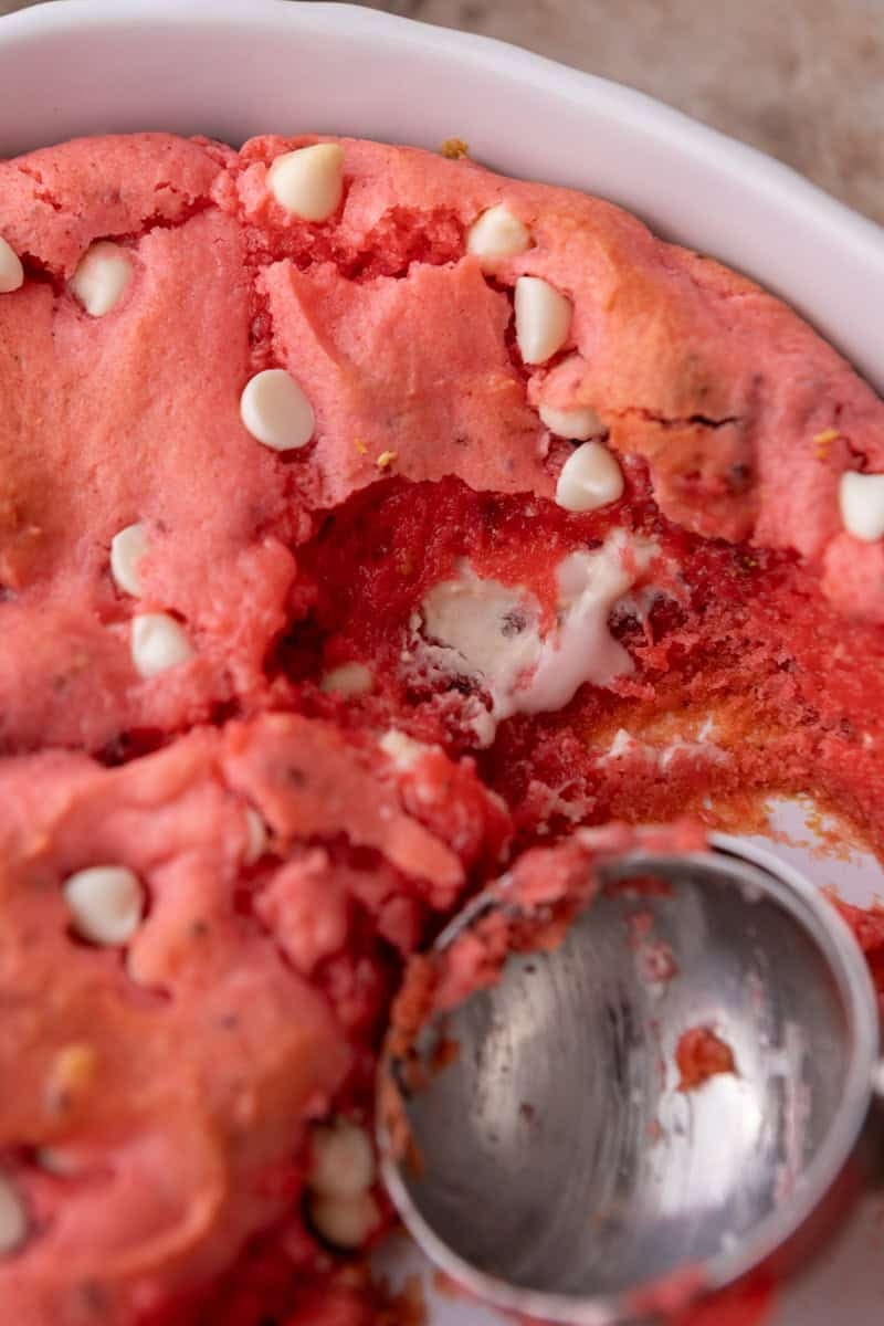 Strawberry scoopable cookies being scooped from a baking dish revealing a soft gooey center