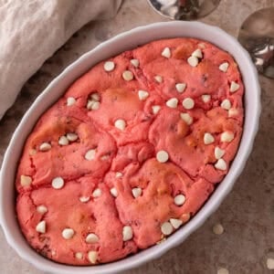 Freshly baked strawberry scoopable cookies in a white oval baking dish with white chocolate chips on top