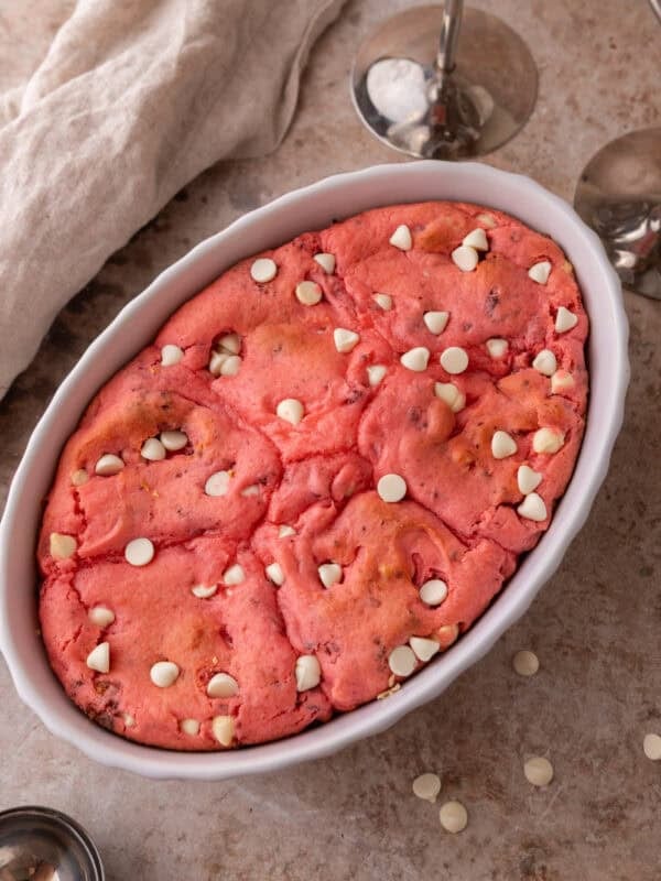 Freshly baked strawberry scoopable cookies in a white oval baking dish with white chocolate chips on top