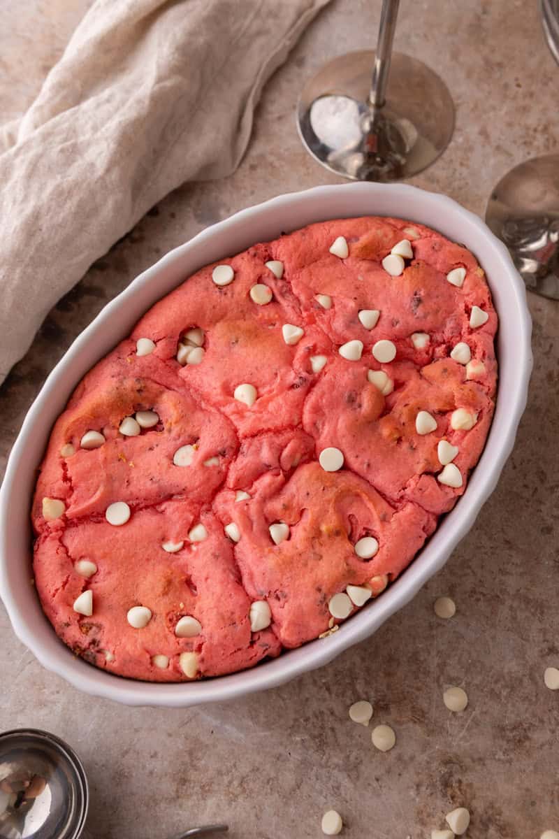 Freshly baked strawberry scoopable cookies in a white oval baking dish with white chocolate chips on top