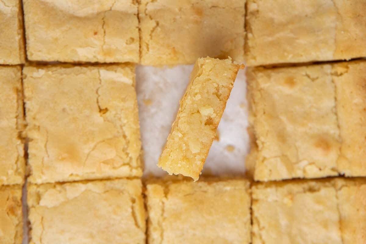 White chocolate brownies sliced into squares with one piece tilted to show the dense fudgy golden interior and crinkly top