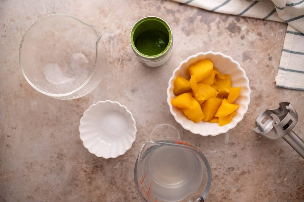ingredients for mango matcha drink with fresh mango chunks coconut water and immersion blender