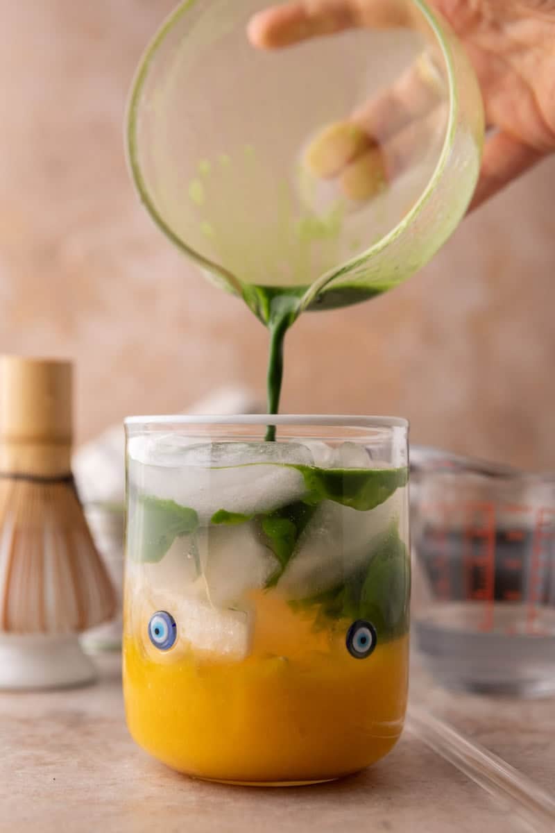 pouring whisked matcha into mango matcha drink creating a layered marble effect