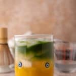 iced mango matcha drink with coconut water in a glass with golden mango and green matcha layers