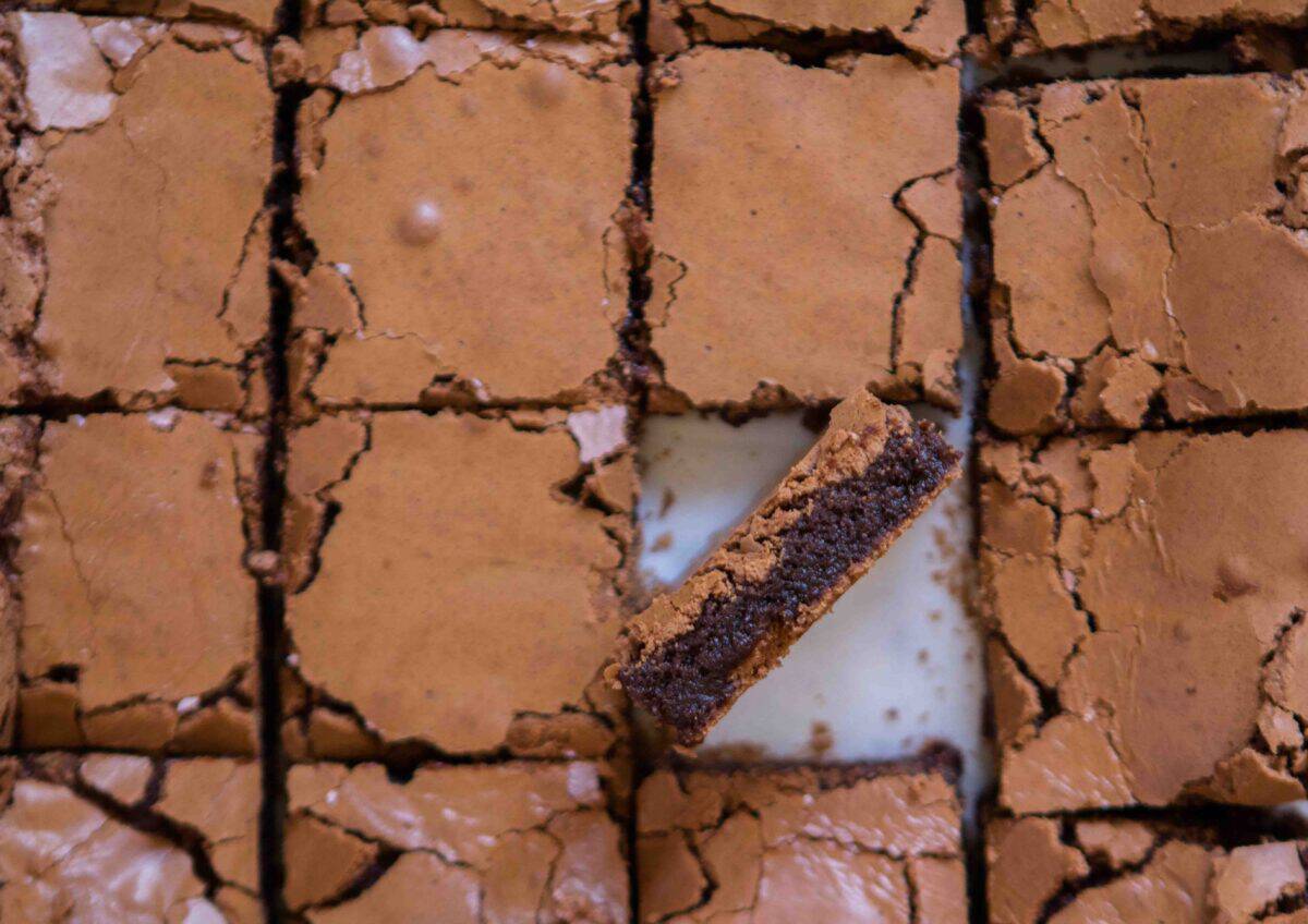 Overhead view of chewy cocoa powder brownies sliced into squares with one piece tilted to show the thick fudgy center and crinkly meringue-like top