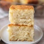 Two butter swim biscuits stacked on a small white plate showing their golden brown tops and soft fluffy interior with the rest of the batch visible in a glass baking dish in the background.