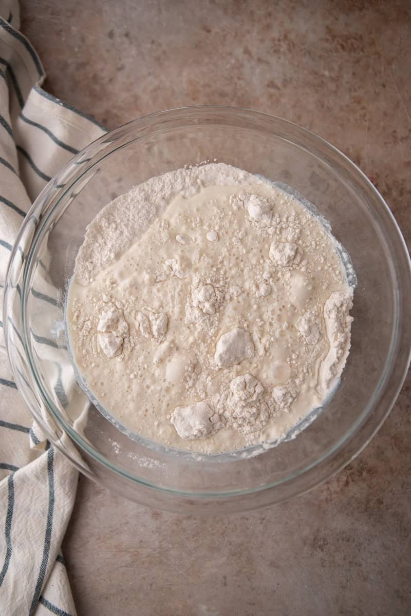 Overhead view of a glass mixing bowl with buttermilk poured over dry ingredients showing the wet and dry components before mixing.