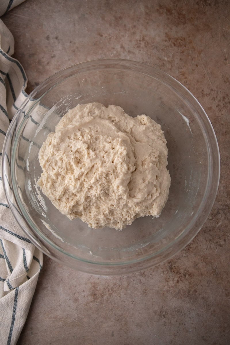 Overhead view of a glass mixing bowl with thick biscuit batter that has been stirred together showing a shaggy, wet dough texture.