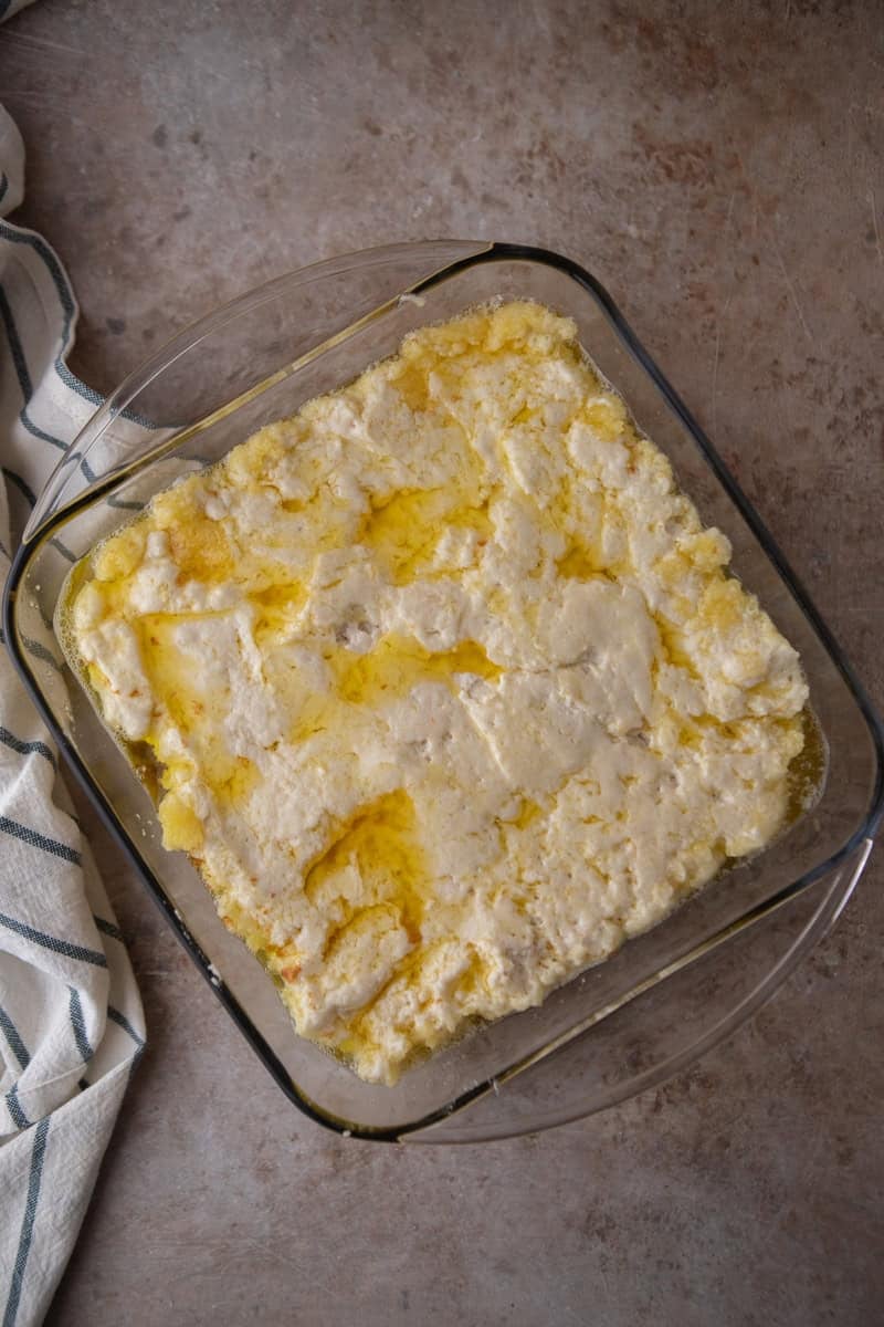 Overhead view of batter spread over melted butter in a glass 8x8 baking dish with golden melted butter visible around the edges and seeping through the batter.